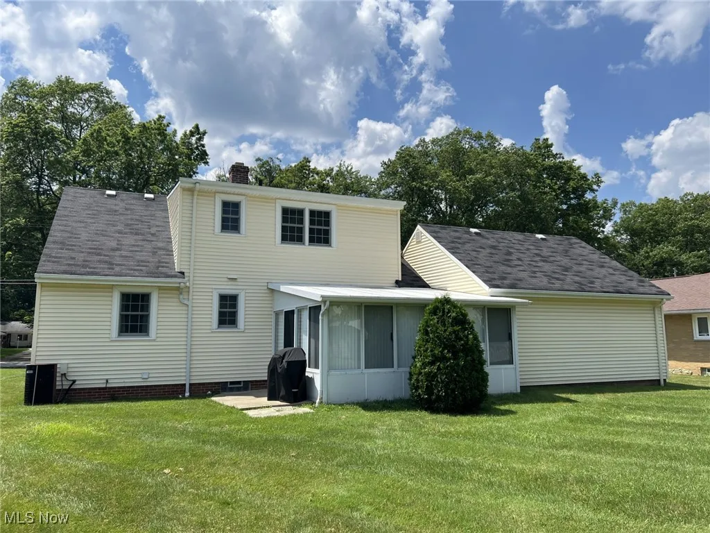 Back of property featuring a sunroom, a yard, a chimney, and a shingled roof
