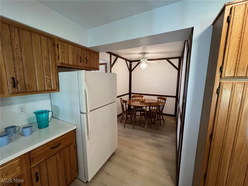 Kitchen with brown cabinetry, freestanding refrigerator, light countertops, light wood-type flooring, and a ceiling fan