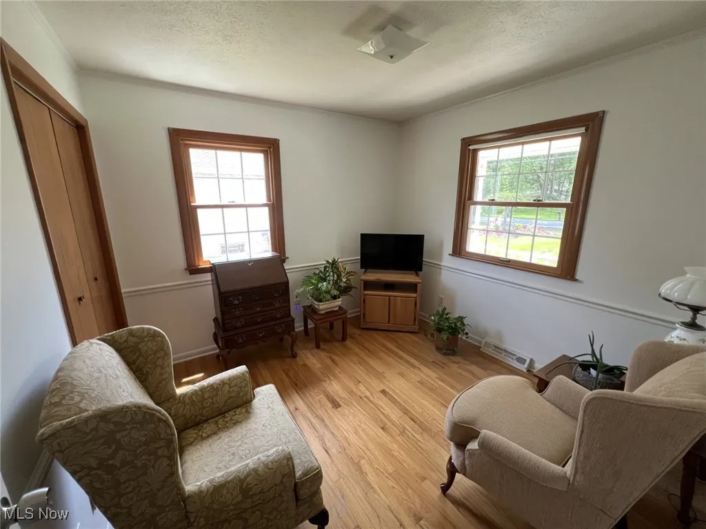 Living area featuring light wood-style flooring, a textured ceiling, and crown molding