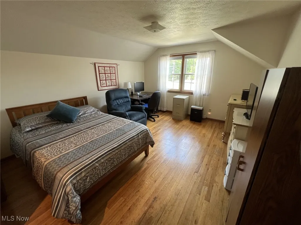 Bedroom with a textured ceiling, lofted ceiling, light wood finished floors, and a desk