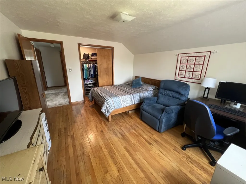 Bedroom featuring a textured ceiling, light wood-type flooring, lofted ceiling, and an office area