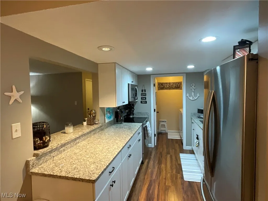 Kitchen featuring appliances with stainless steel finishes, white cabinets, dark wood-style flooring, light stone countertops, and recessed lighting