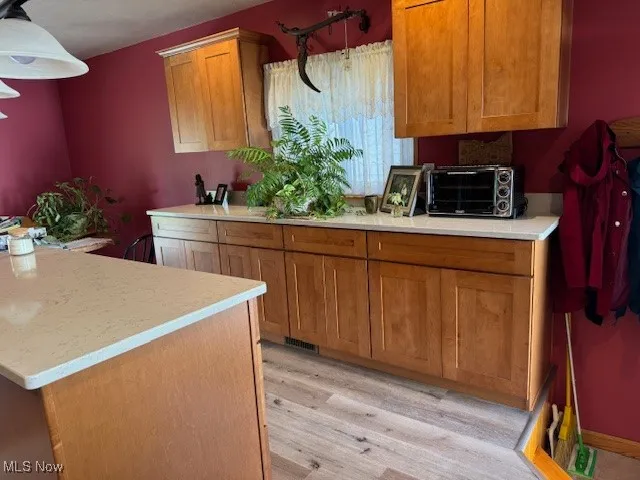 Kitchen with brown cabinets, light wood-style flooring, decorative light fixtures, and light  quartz countertops