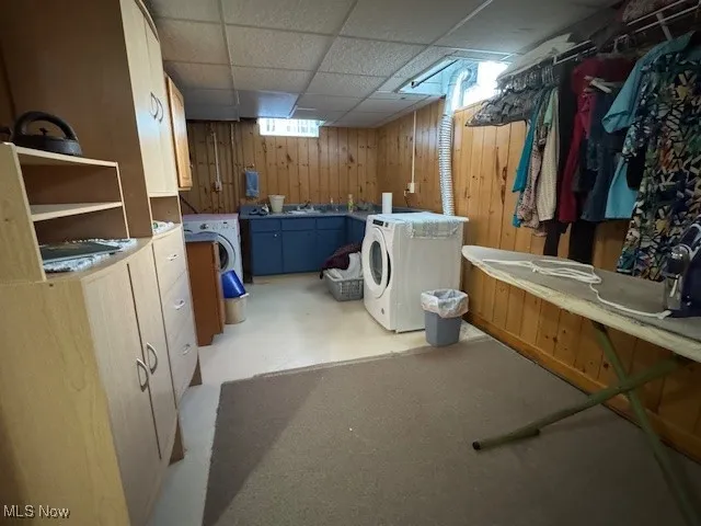 Laundry area featuring a drop ceiling, cabinet space, washer and clothes dryer, and wooden walls