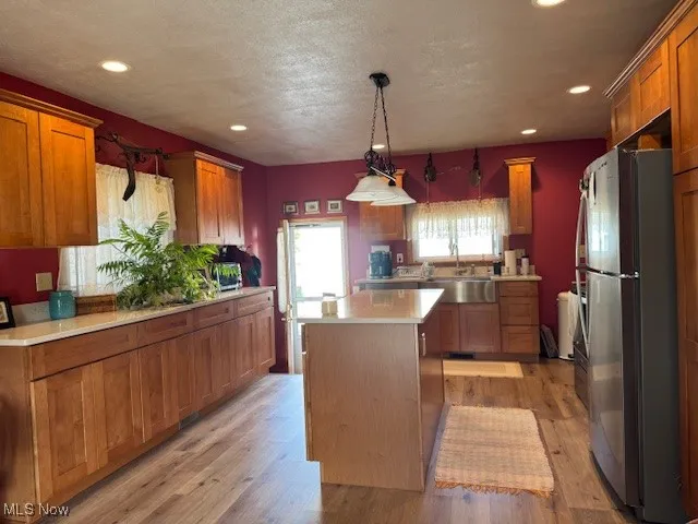 Kitchen featuring brown cabinetry, freestanding refrigerator, light wood-style flooring, decorative light fixtures, and recessed lighting