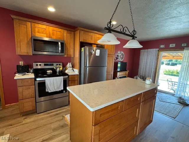 Kitchen with stainless steel appliances, hanging light fixtures, brown cabinets, light wood-type flooring, and a center island