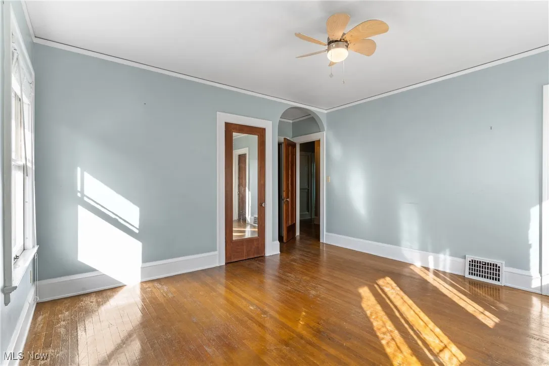 Spare room featuring wood-type flooring, crown molding, arched walkways, and ceiling fan