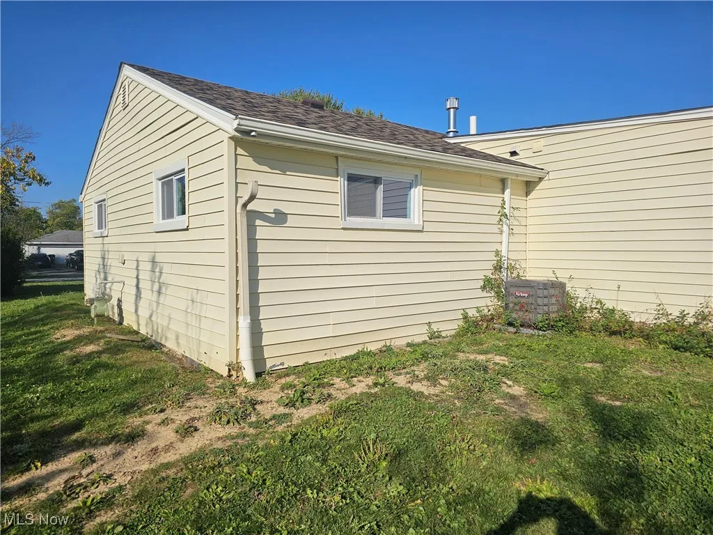 View of property exterior with a yard and roof with shingles