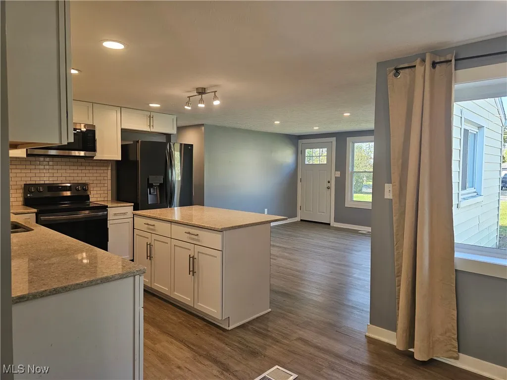 Kitchen with black appliances, light stone counters, laminate flooring, and recessed lighting