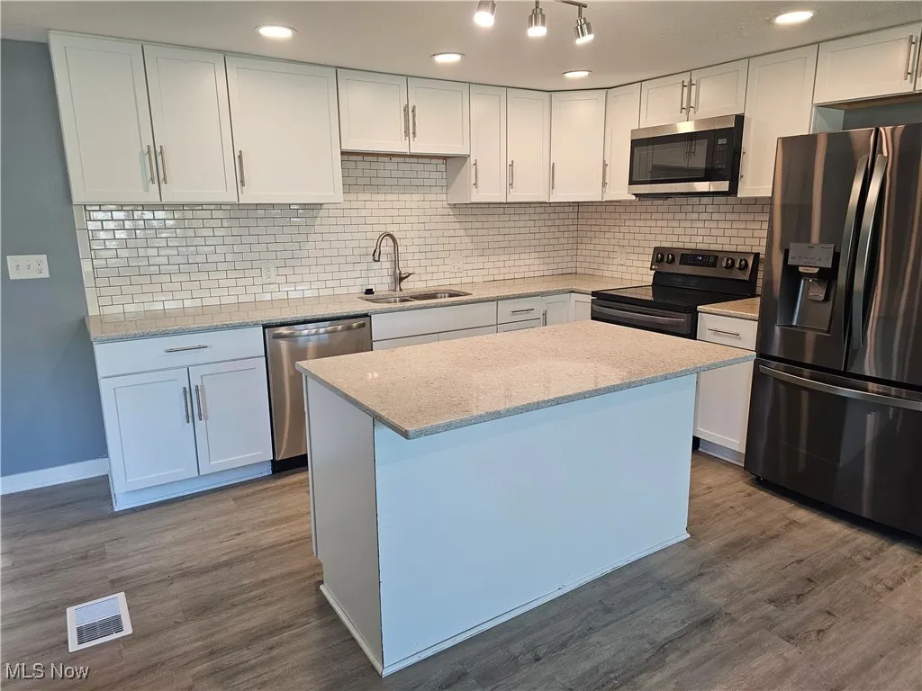 Kitchen with appliances with stainless steel finishes, white cabinetry, decorative backsplash, light stone countertops, and a center island
