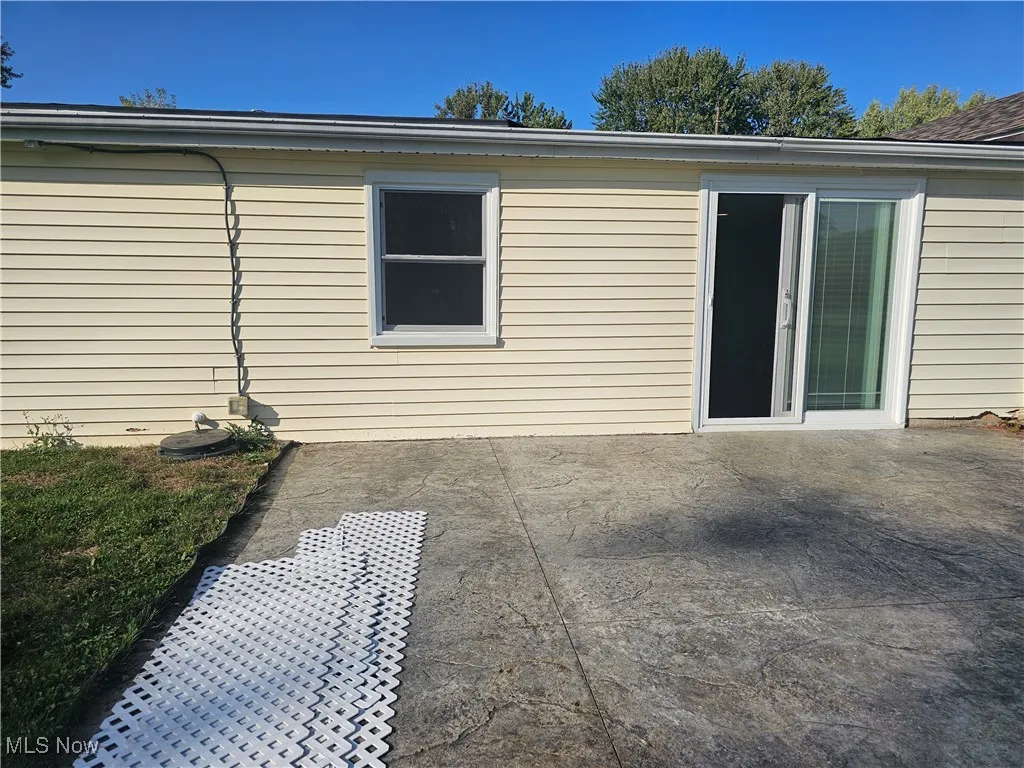 Concrete patio in this large fenced back yard and more yard beyond the fence.