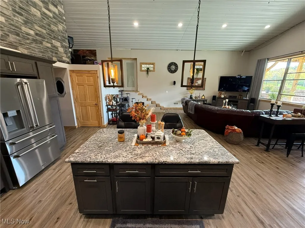 Kitchen with high end refrigerator, light wood finished floors, light stone counters, hanging light fixtures, and a kitchen island