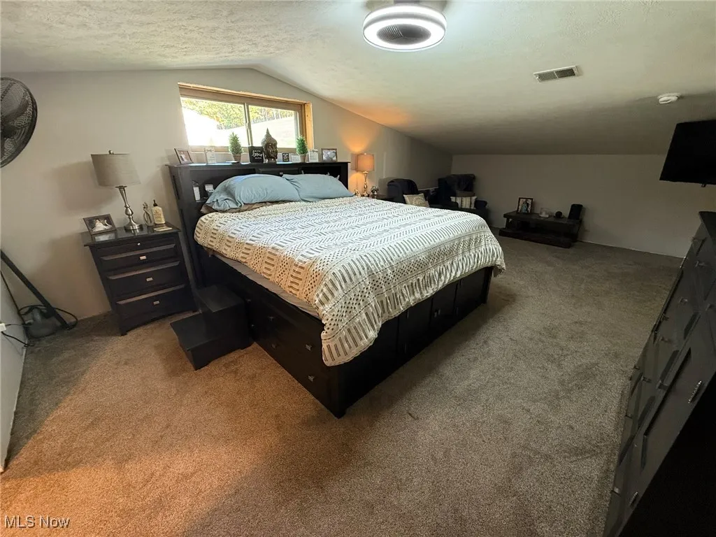 Carpeted bedroom featuring a textured ceiling and lofted ceiling