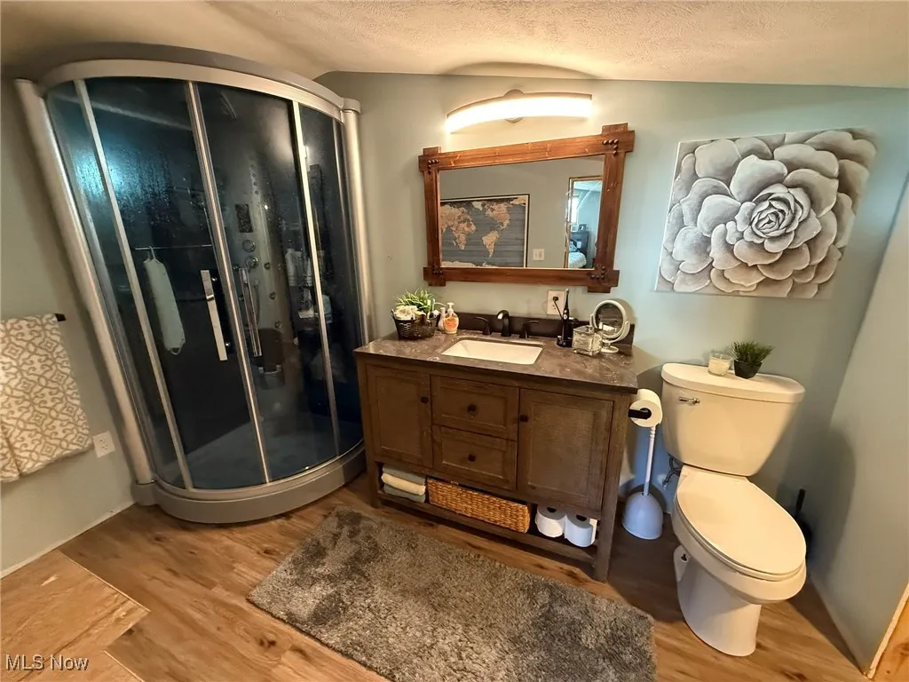 Bathroom featuring a shower stall, vanity, a textured ceiling, and light wood-type flooring
