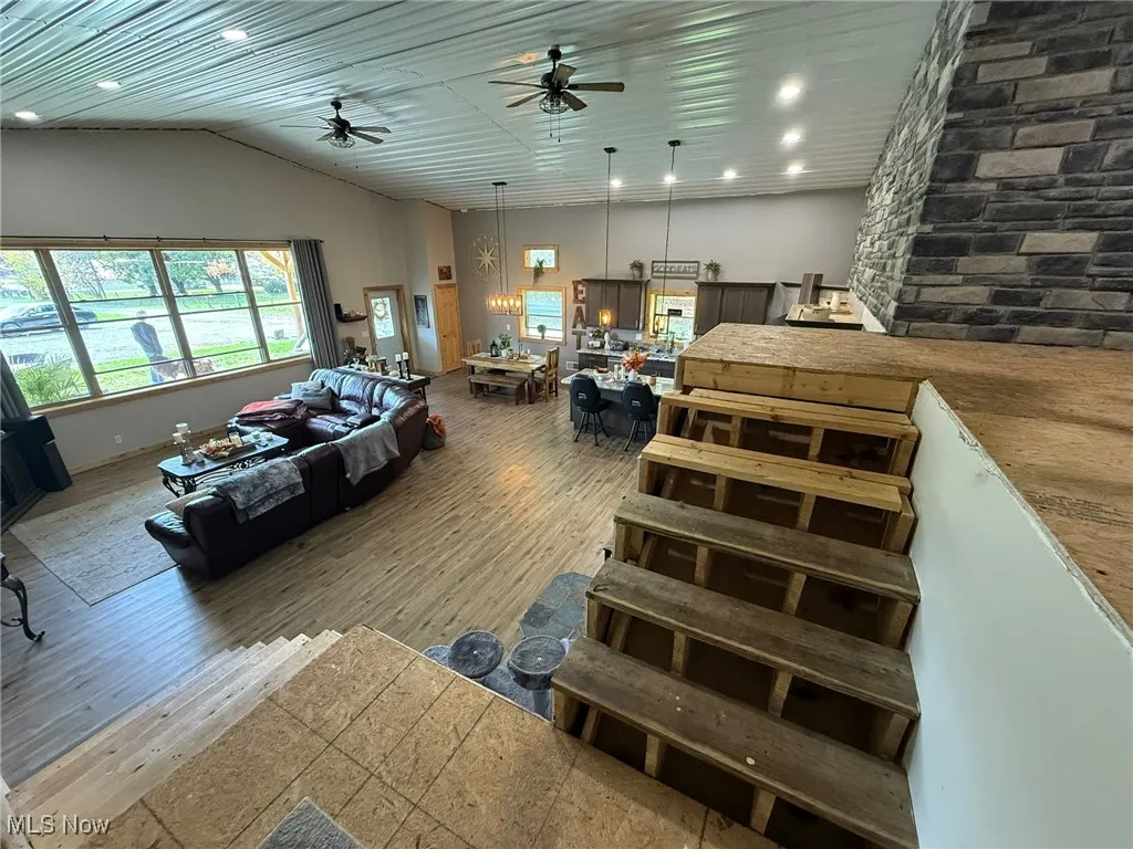 Living room featuring ceiling fan, wood finished floors, lofted ceiling, and a chandelier