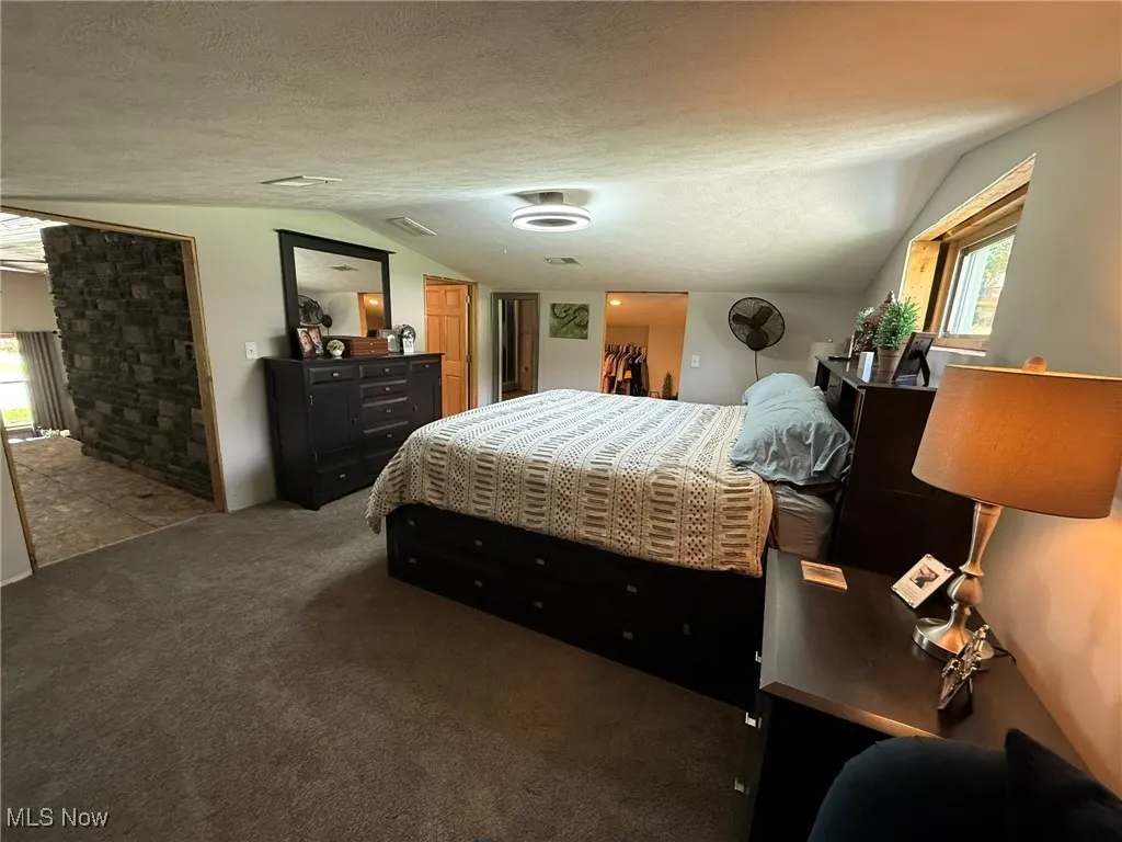 Carpeted bedroom featuring a textured ceiling and vaulted ceiling