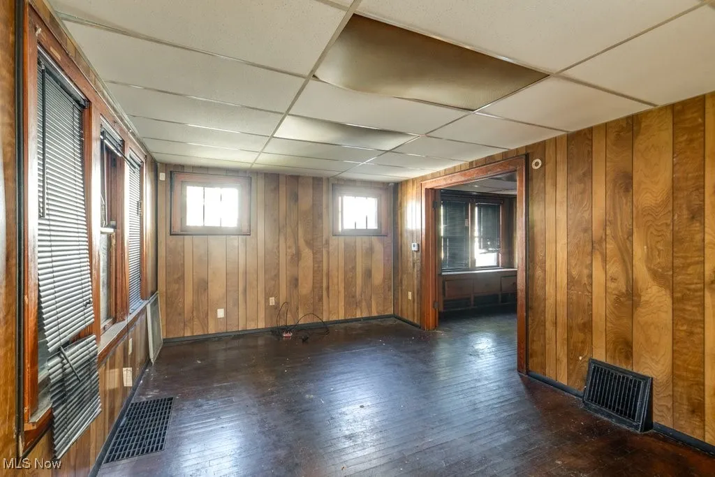 Empty room with a drop ceiling, dark wood-style floors, and wooden walls