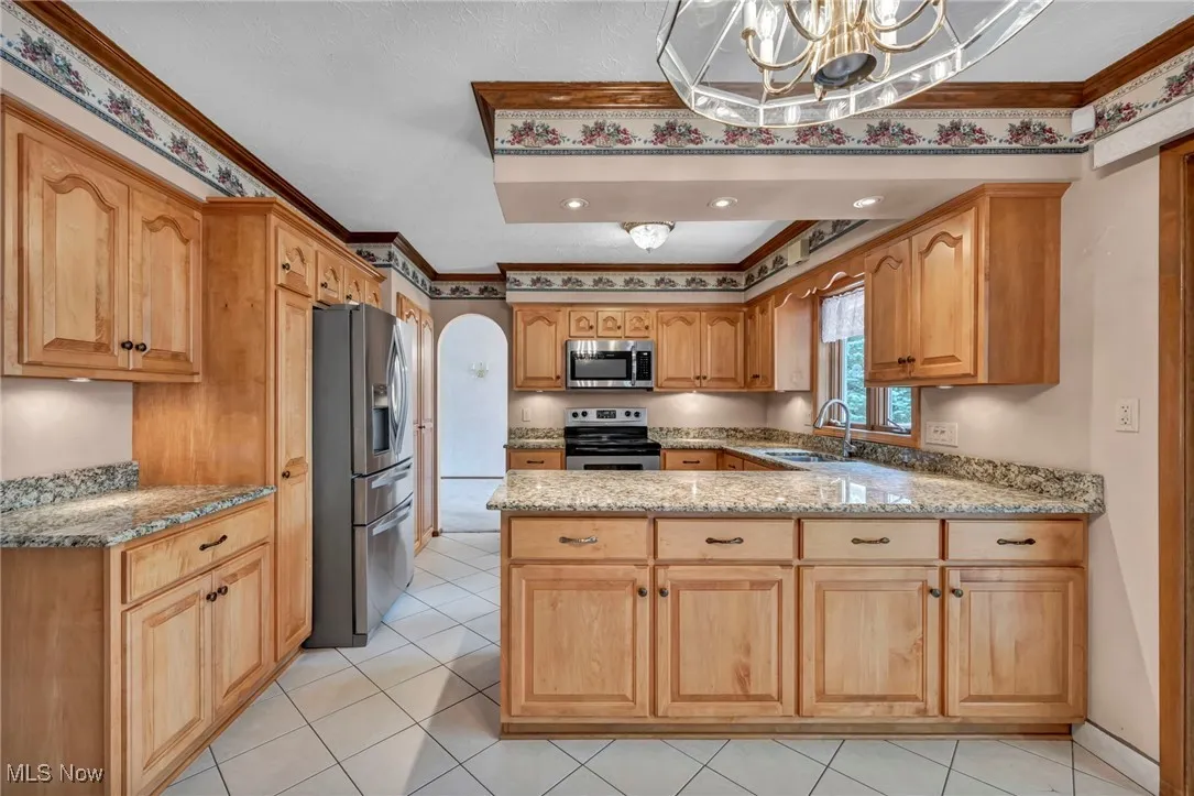 Kitchen with light tile patterned floors, light stone counters, appliances with stainless steel finishes, arched walkways, and ornamental molding