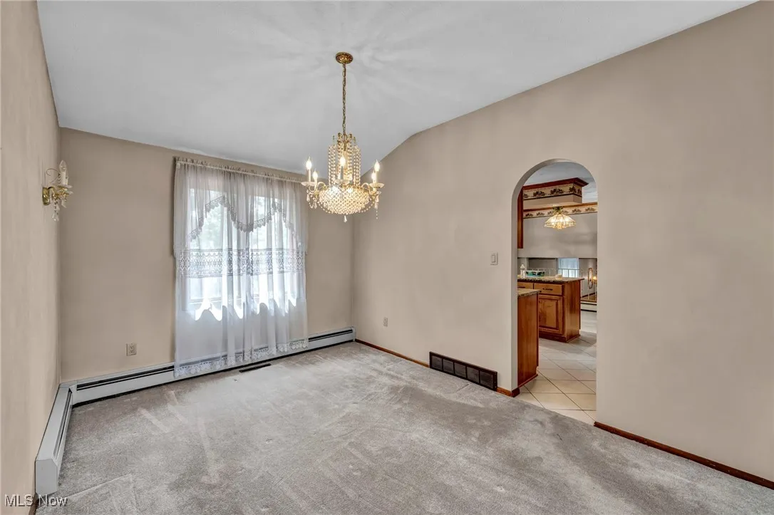 Unfurnished dining area with a chandelier, light colored carpet, arched walkways, vaulted ceiling, and baseboard heating