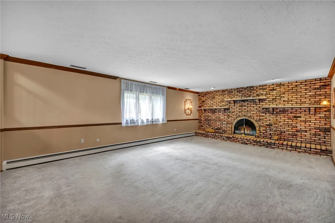 Unfurnished living room featuring crown molding, a baseboard radiator, carpet flooring, brick wall, and a textured ceiling