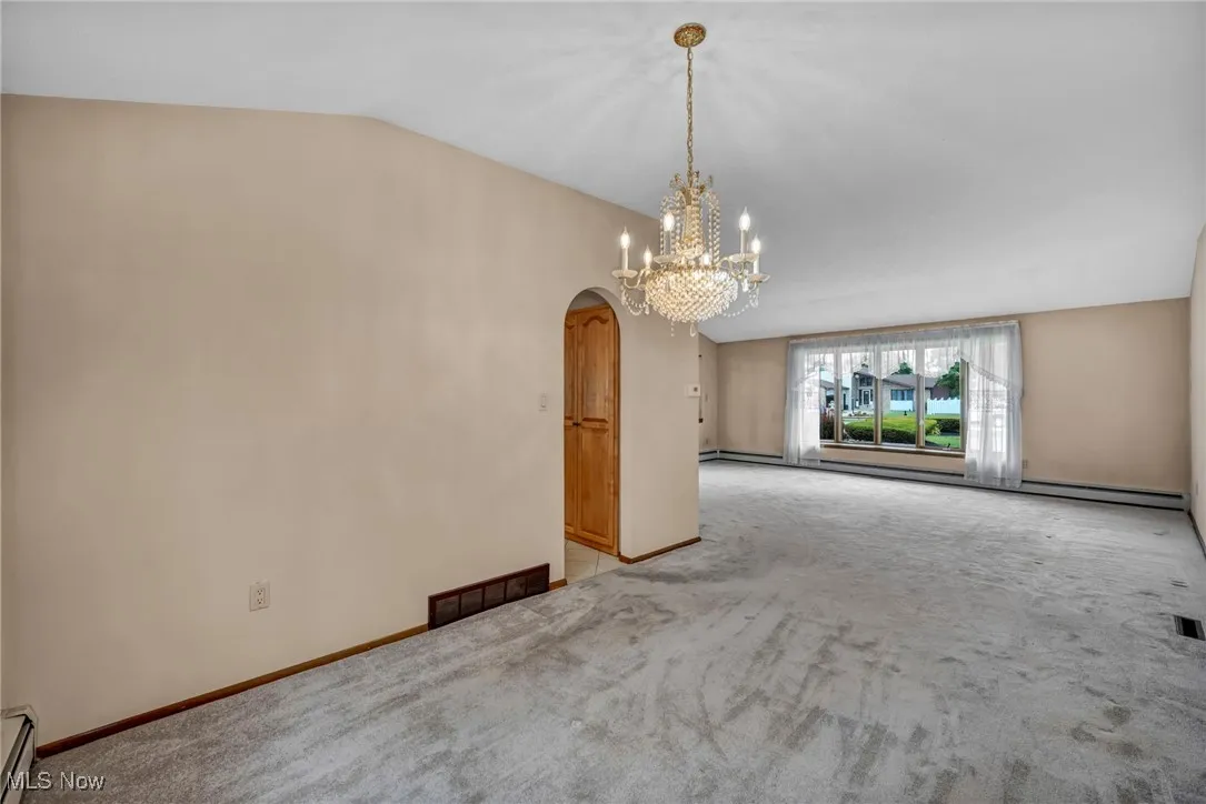 Unfurnished dining area featuring arched walkways, lofted ceiling, carpet flooring, a chandelier, and baseboard heating