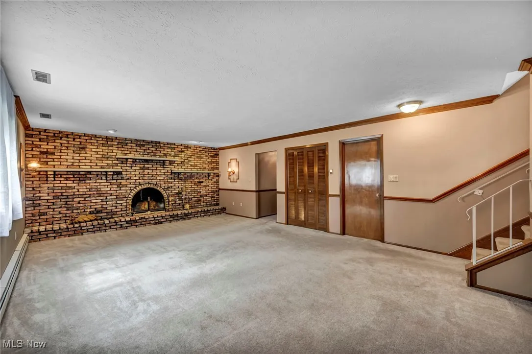 Unfurnished living room with carpet flooring, crown molding, a baseboard radiator, a textured ceiling, and a fireplace