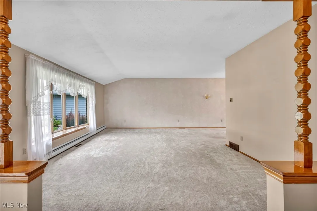 Unfurnished living room with lofted ceiling, a baseboard heating unit, carpet floors, and a textured ceiling