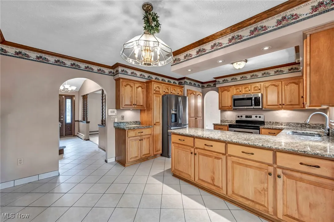 Kitchen featuring arched walkways, light stone countertops, a chandelier, appliances with stainless steel finishes, and crown molding