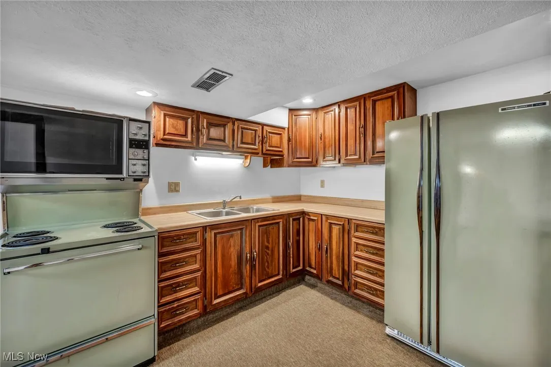 Kitchen featuring freestanding refrigerator, range with electric stovetop, light countertops, stainless steel microwave, and a textured ceiling