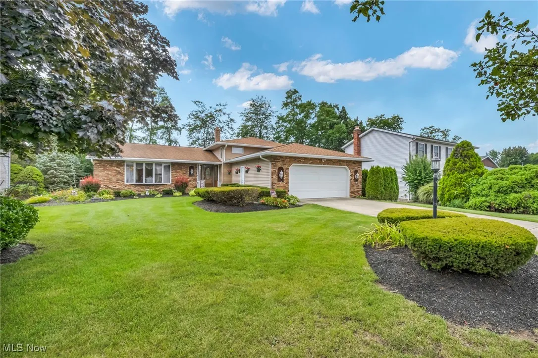 View of front of property featuring concrete driveway, a front yard, an attached garage, a chimney, and brick siding