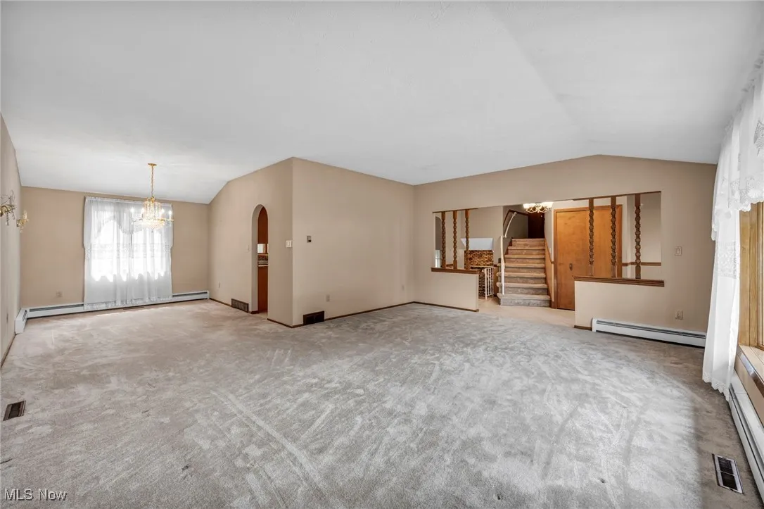 Unfurnished living room featuring a chandelier, vaulted ceiling, stairs, and a baseboard heating unit