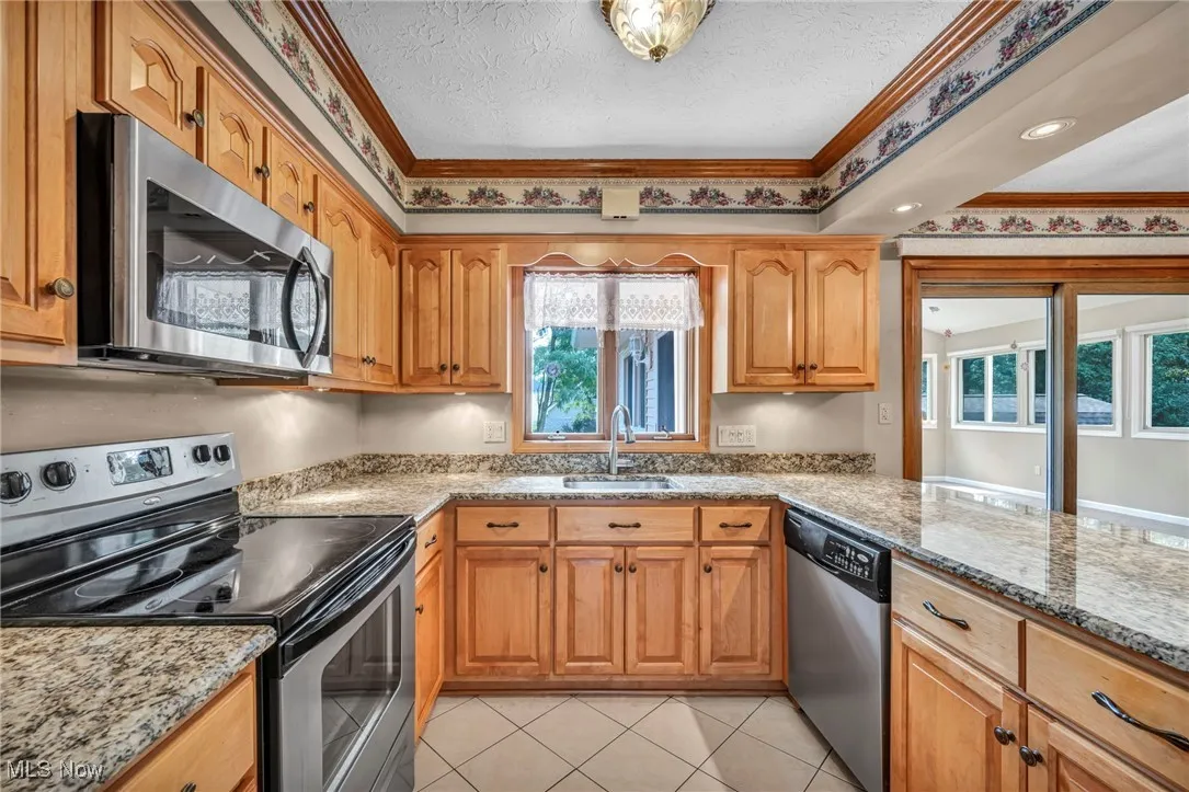 Kitchen featuring stainless steel appliances, light tile patterned floors, light stone countertops, a textured ceiling, and brown cabinetry