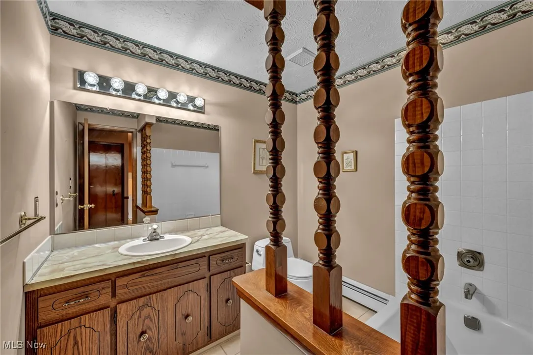 Full bathroom featuring vanity, light tile patterned floors, a baseboard radiator, and a textured ceiling