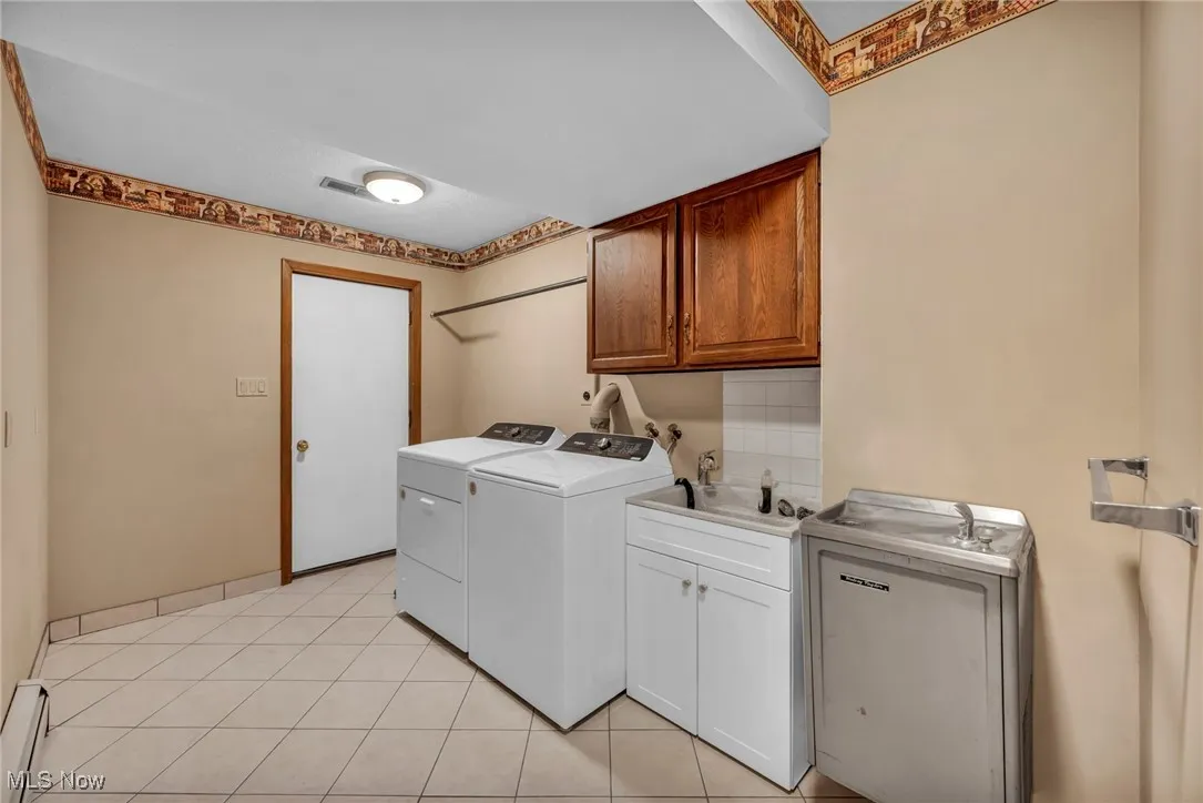 Laundry area featuring cabinet space, light tile patterned flooring, independent washer and dryer, and a baseboard heating unit