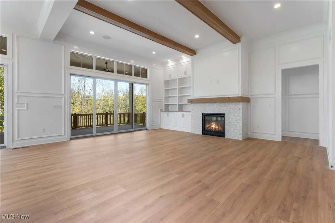 Unfurnished living room with a decorative wall, beamed ceiling, a glass covered fireplace, light wood-type flooring, and recessed lighting