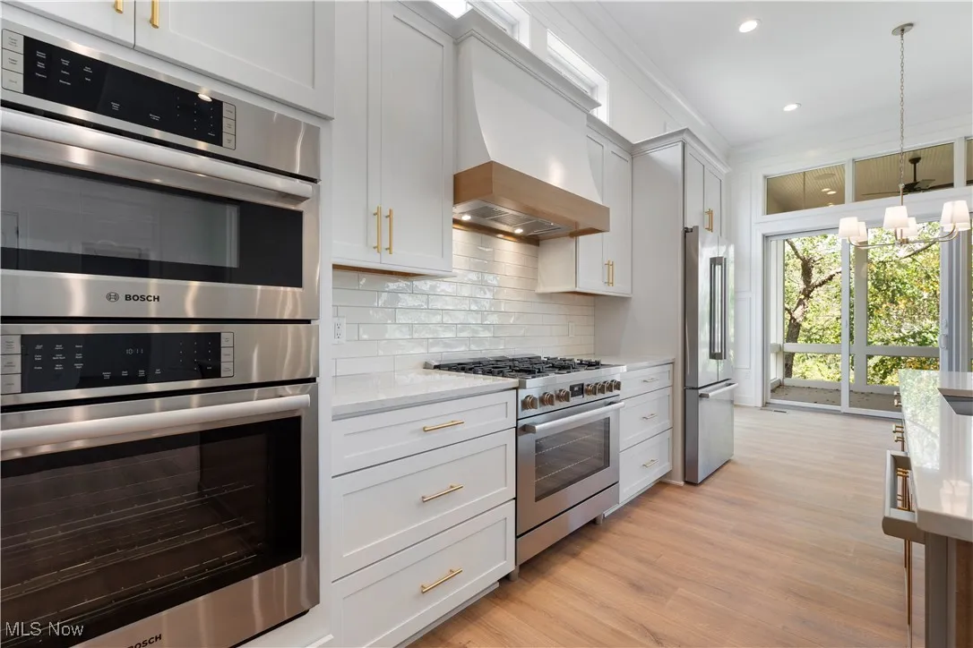 Kitchen with appliances with stainless steel finishes, white cabinets, a chandelier, decorative light fixtures, and custom range hood