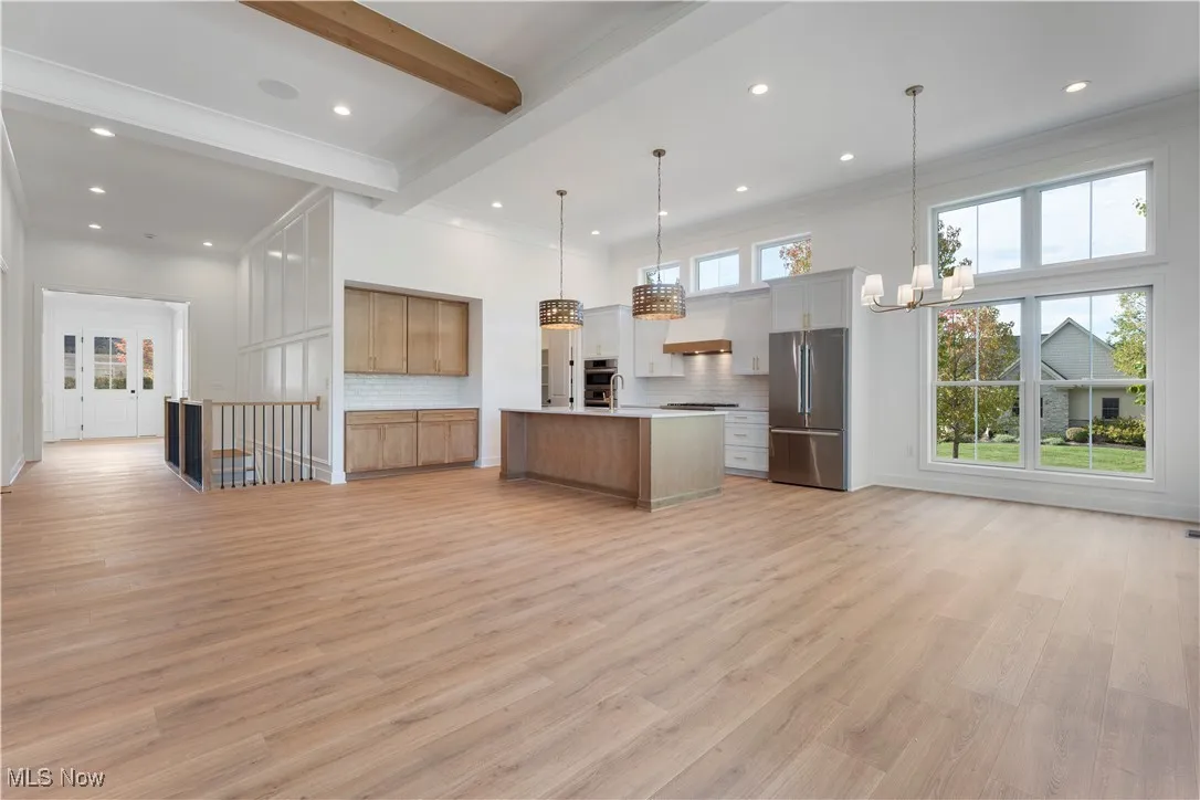 Kitchen featuring open floor plan, beam ceiling, decorative backsplash, appliances with stainless steel finishes, and pendant lighting