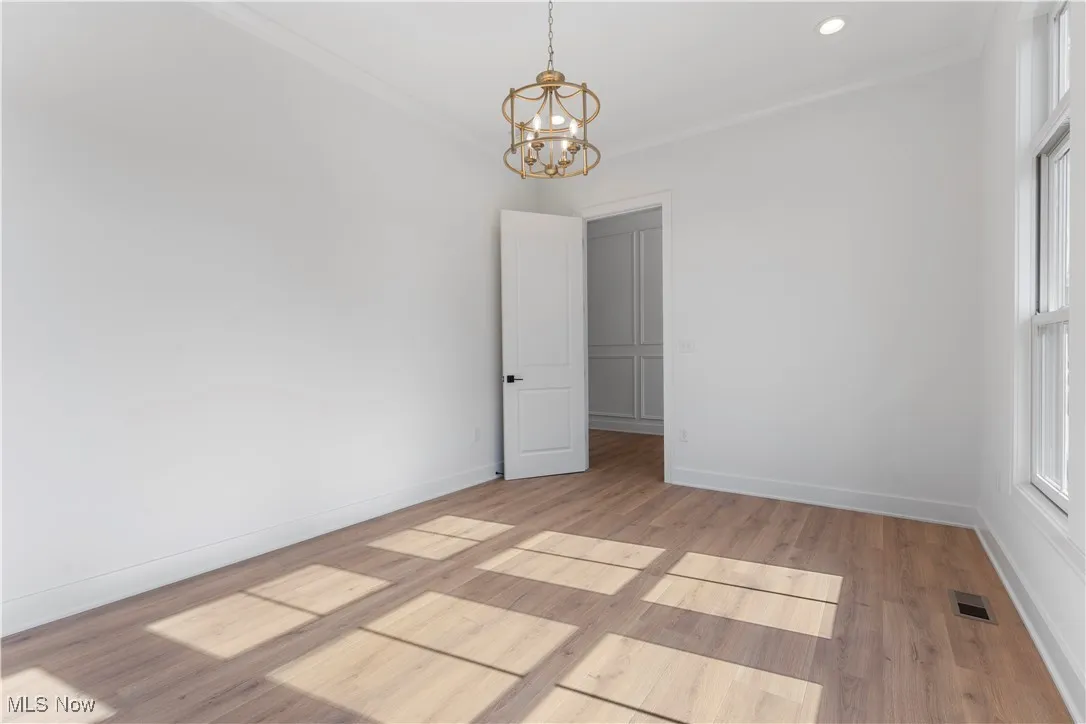 Empty room featuring crown molding, a chandelier, light wood-style floors, and recessed lighting