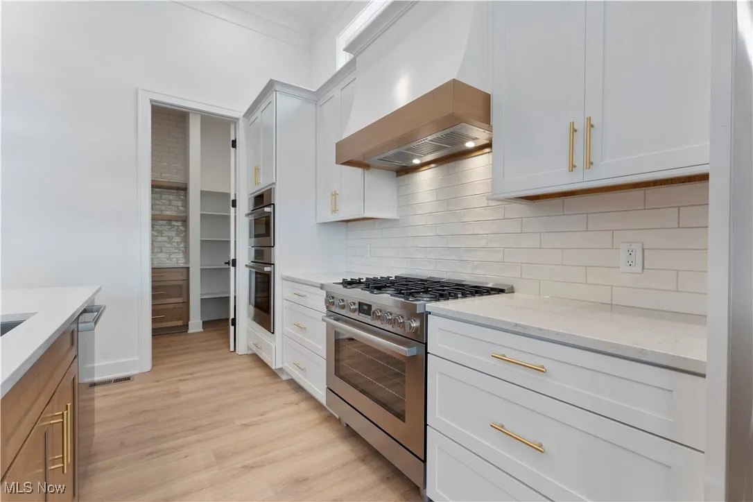 Kitchen with stainless steel appliances, light stone countertops, custom exhaust hood, backsplash, and ornamental molding