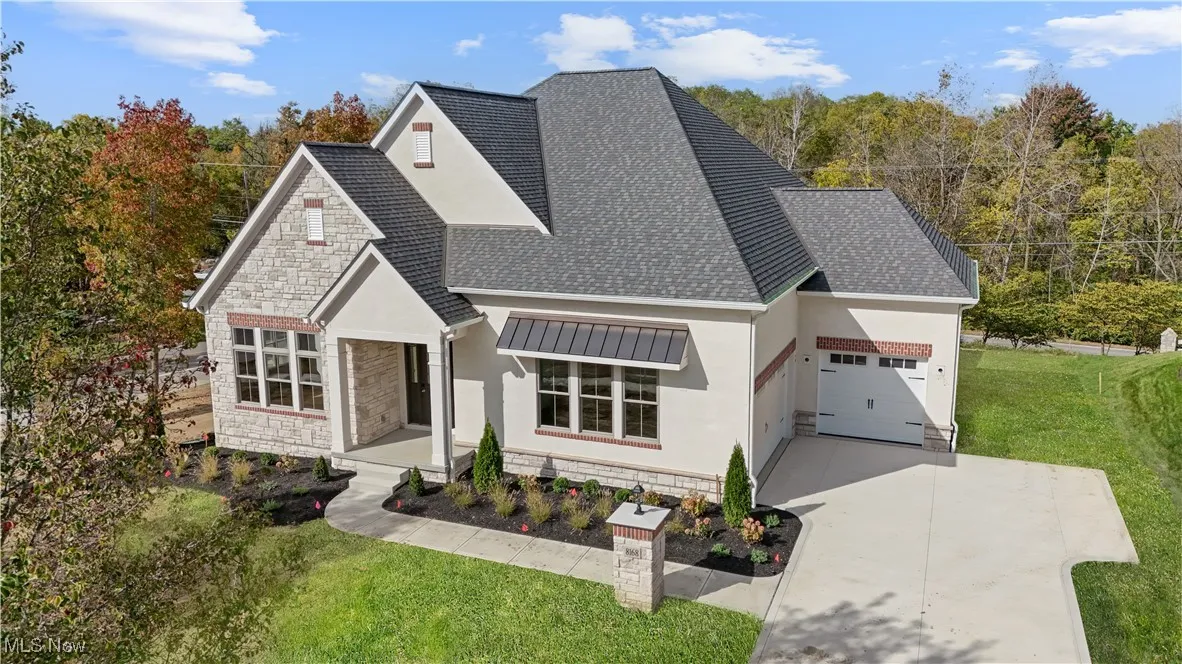 View of front of home with stone siding, a shingled roof, a front yard, and stucco siding