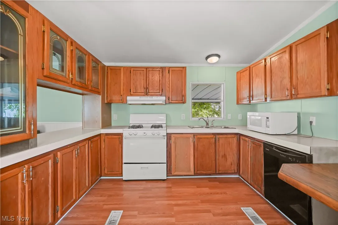 Kitchen featuring white appliances, light countertops, light wood-type flooring, glass insert cabinets, and brown cabinetry