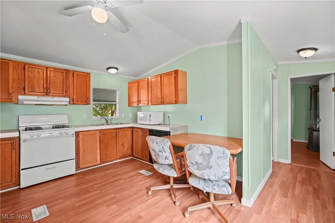 Kitchen with white appliances, light wood-style floors, crown molding, light countertops, and under cabinet range hood