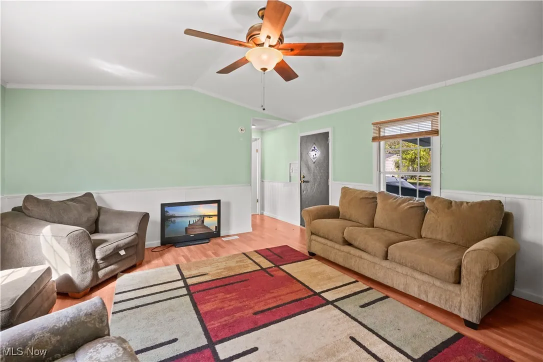 Living area with ornamental molding, wood finished floors, vaulted ceiling, ceiling fan, and wainscoting
