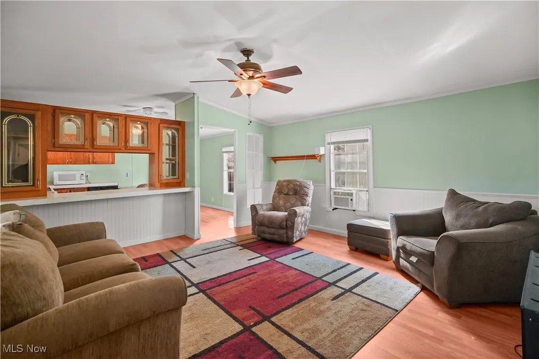 Living area featuring light wood finished floors, lofted ceiling, ceiling fan, and ornamental molding