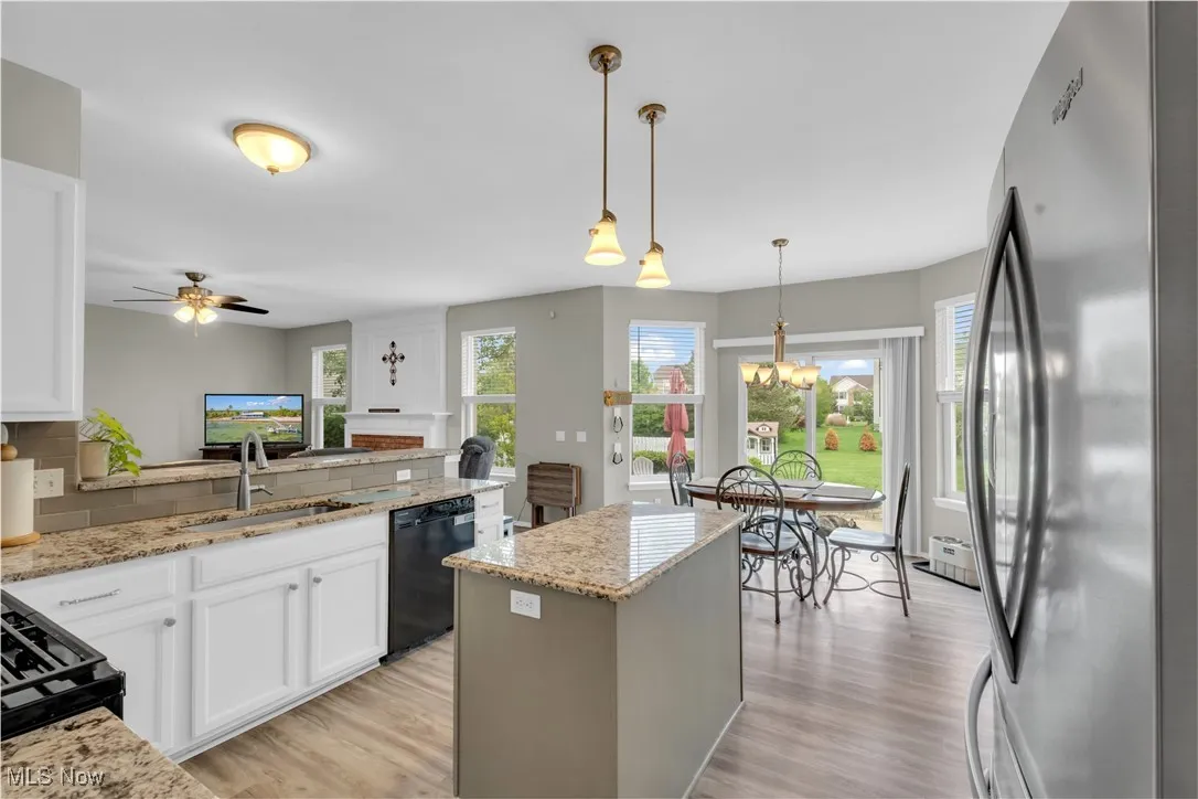 Kitchen with black appliances, a peninsula, light wood finished floors, light stone counters, and hanging light fixtures