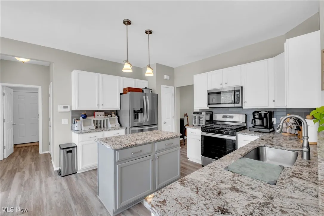Kitchen with decorative backsplash, stainless steel appliances, decorative light fixtures, and white cabinetry