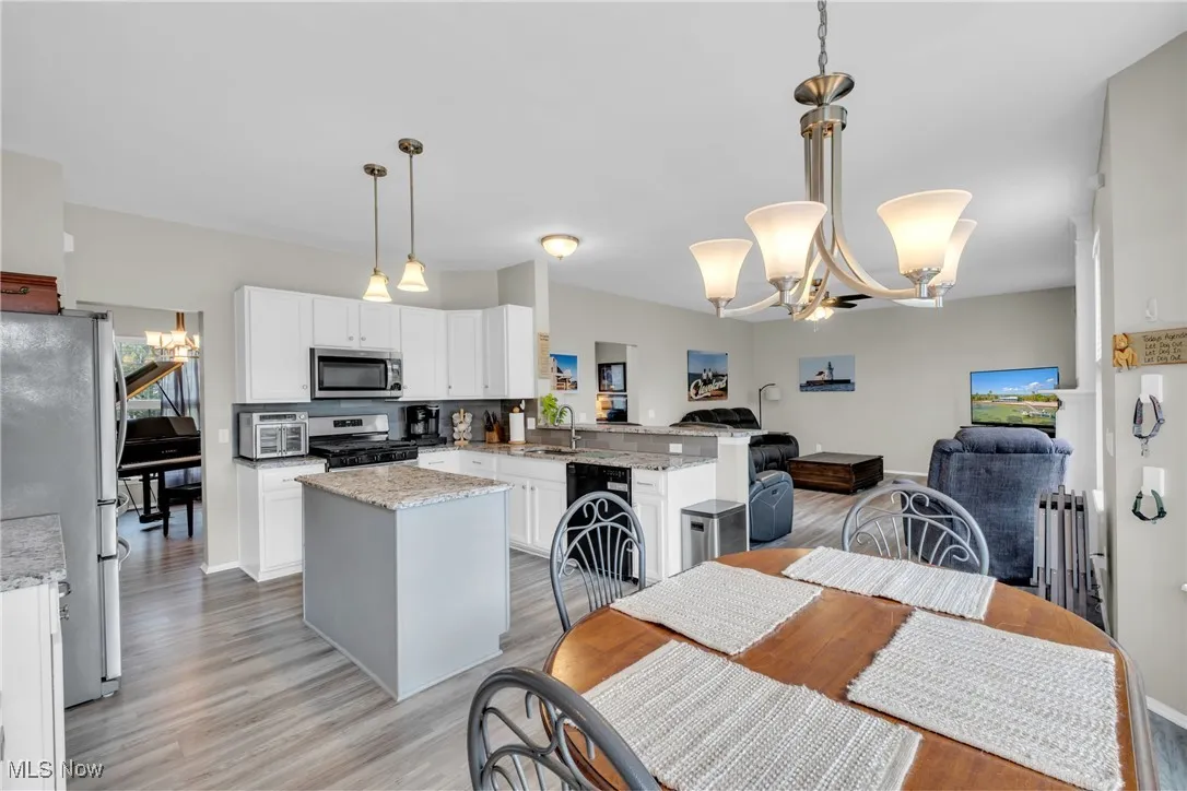 Kitchen featuring a chandelier, stainless steel appliances, light stone countertops, open floor plan, and white cabinetry
