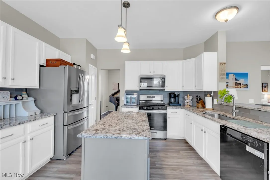 Kitchen featuring appliances with stainless steel finishes, decorative light fixtures, backsplash, light stone counters, and a kitchen island