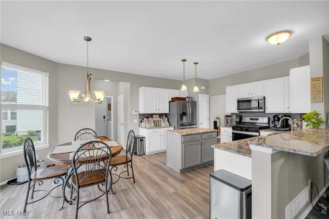 Kitchen with decorative light fixtures, stainless steel appliances, light stone countertops, a chandelier, and light wood-style flooring