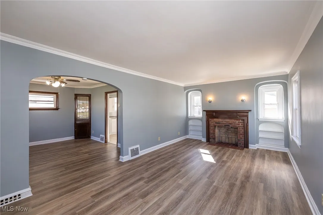 Unfurnished living room with ornamental molding, plenty of natural light, a fireplace, and dark wood finished floors